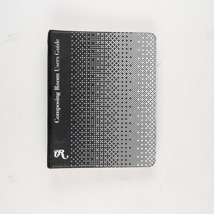 Op de afbeelding: Een zwart boek getiteld "Composing Room Users Guide" met een wit stippenpatroon op de omslag. Het boek heeft de letter "R" in een gestileerd lettertype in de linker benedenhoek. Het boek staat op een witte achtergrond.