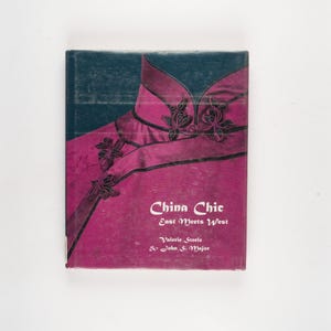 May include: A book titled "China Chic East Meets West" with a cover featuring a magenta and black design. The cover art depicts a stylized Chinese garment with floral accents. The book's title and author's names are printed in white.