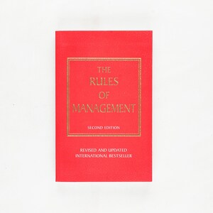 May include: A red book titled "The Rules of Management" with gold lettering. The book is a second edition, revised and updated, and an international bestseller. The book is on a white background.