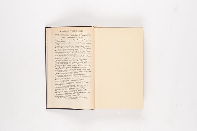 May include: An open book with a dark cover, displaying text on the left page and a blank cream-colored page on the right. The text is a list of names under the title "AMERICAN WRITERS SERIES". The book is set against a white background.