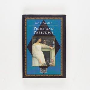 Op de afbeelding: Een hardcover editie van "Pride and Prejudice" van Jane Austen. Het boek heeft een blauwe kaft met gouden details en een afbeelding van een vrouw in een witte jurk. Het Barnes & Noble Classics-logo staat onderaan.