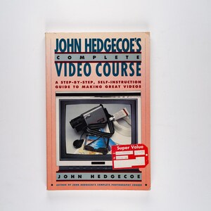 May include: A pink and blue book titled "John Hedgecoe's Complete Video Course: A Step-by-Step, Self-Instruction Guide to Making Great Videos". The cover features a vintage camcorder in front of a television screen.