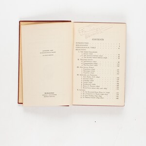 May include: An open book with a red cover and cream-colored pages. The left page has text, including the year 1935. The right page displays a table of contents. The book is on a white surface.