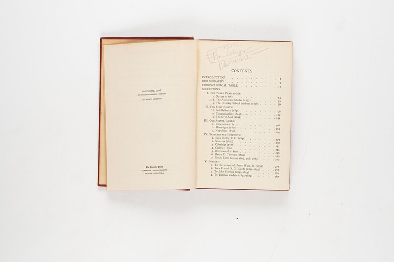 May include: An open book with a red cover and cream-colored pages. The left page has text, including the year 1935. The right page displays a table of contents. The book is on a white surface.