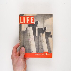 Może przedstawiać: Okładka vintage magazynu LIFE z 23 listopada 1936 roku, przedstawiająca czarno-białe zdjęcie dużego budynku z tekstem "LIFE" w czerwonych literach i "10 CENTS" w czerwonych literach na dole.