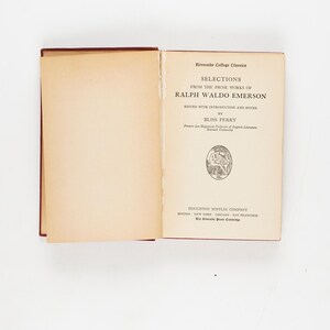 May include: An open book titled "Selections from the Prose Works of Ralph Waldo Emerson" with text in black font. The book is part of the Riverside College Classics series. The book's pages are off-white, and the cover is a dark red.