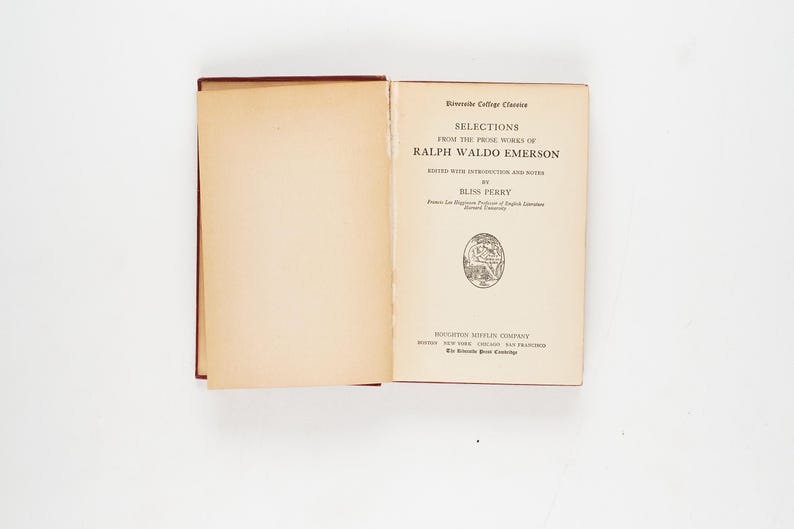 May include: An open book titled "Selections from the Prose Works of Ralph Waldo Emerson" with text in black font. The book is part of the Riverside College Classics series. The book's pages are off-white, and the cover is a dark red.