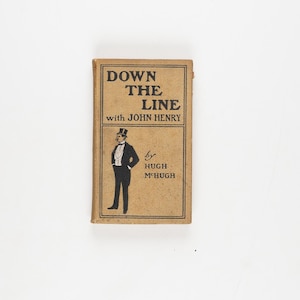 May include: A vintage book titled "Down the Line with John Henry" by Hugh McHugh. The cover is a light brown colour with black text and a black illustration of a man in a tuxedo. The book is rectangular and appears to be in good condition.