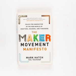 May include: A hardcover book titled "The Maker Movement Manifesto" with colorful lettering. The book's cover is white with text in black, orange, blue, and green. The author's name and the CEO of Techshop are also printed on the cover.