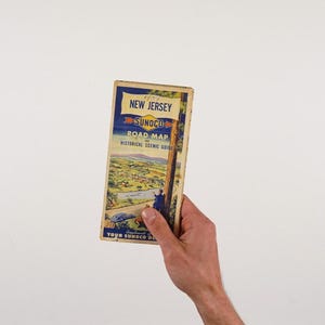 May include: A vintage New Jersey Sunoco road map and historical scenic guide. The cover features a blue banner with the words "New Jersey" and "Road Map". The map shows a scenic view of a town and a river.