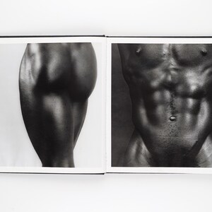 May include: A monochrome photograph of an open book. One page displays a close-up of a leg, the other a torso. The images are detailed and artistic, with strong contrasts and shadows.