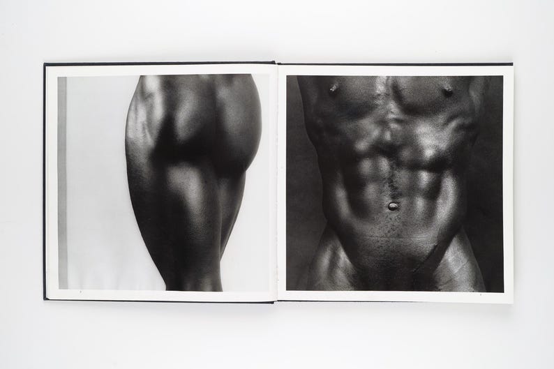 May include: A monochrome photograph of an open book. One page displays a close-up of a leg, the other a torso. The images are detailed and artistic, with strong contrasts and shadows.