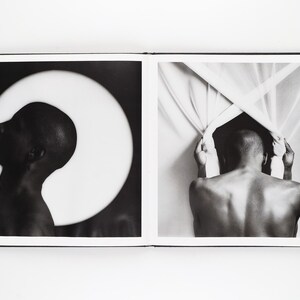 May include: A monochrome photograph showing a person's profile against a bright white circle, and a person's back pulling back a curtain. The images are in a book with a white border and black frame.