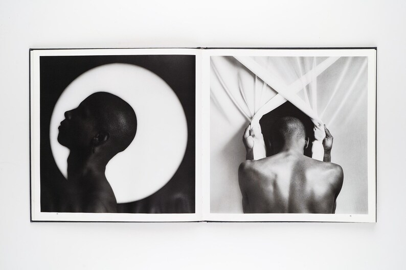 May include: A monochrome photograph showing a person's profile against a bright white circle, and a person's back pulling back a curtain. The images are in a book with a white border and black frame.