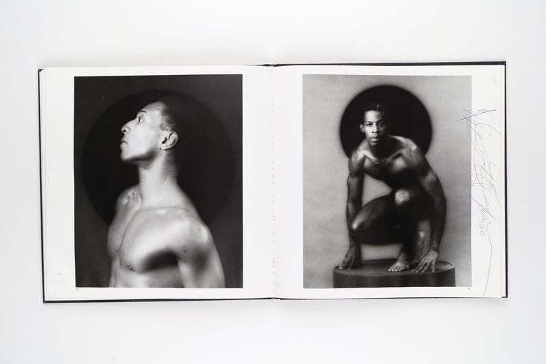 May include: A monochrome photograph displayed across two pages of a book. One image shows a man looking upwards, the other a man crouching. Each image features a dark circular backdrop.