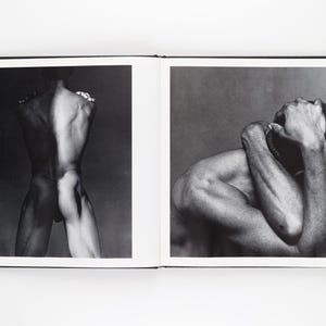 May include: A monochrome photograph in a book, showing two images. One depicts a nude figure's back, the other a person with arms around their head. The images are in black and white.