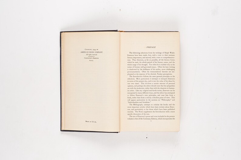 May include: An open book with black covers, lying flat on a white surface. The left page has text from the American Book Company, and the right page has the title "Preface". The book is a vintage edition.