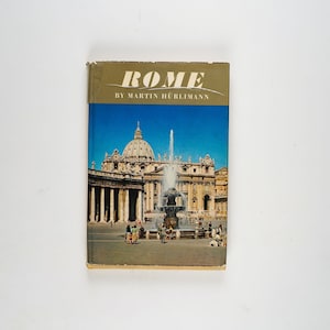 Pode incluir: Um livro intitulado "ROMA" de Martin Hürlimann com uma foto da Basílica de São Pedro e uma fonte em primeiro plano.
