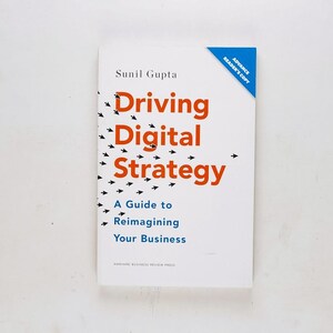 May include: A white book with an orange and black title "Driving Digital Strategy: A Guide to Reimagining Your Business" by Sunil Gupta. The book cover features a design of black arrows pointing towards the title.