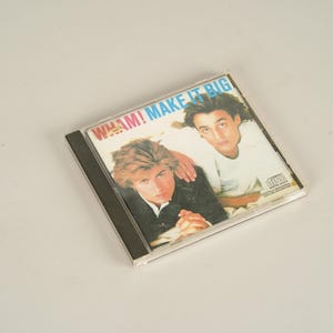 May include: A compact disc case featuring the album "Make It Big" by Wham!. The cover art displays two men, one with his arm on the other's shoulder. The album title is in a colorful font across the top.