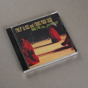 May include: A CD case with a black spine and a clear front cover. The front cover features a photo of two people in red robes walking on a wooden stage. The text on the cover reads "Philip Glass and Foday Musa Suso Music from the Screens".