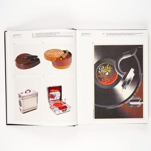 May include: A vintage book spread featuring various antique items. The left page showcases a brown leather case, a wooden container, a small metal box, and a red and silver portable record player. The right page displays a vintage advertisement for Path&eacute; records.