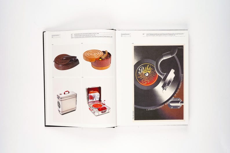 May include: A vintage book spread featuring various antique items. The left page showcases a brown leather case, a wooden container, a small metal box, and a red and silver portable record player. The right page displays a vintage advertisement for Path&eacute; records.