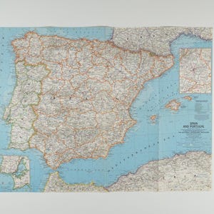 May include: A vintage map of the Iberian Peninsula, including Spain and Portugal, with detailed geographical features. The map features a light blue ocean and landmasses in shades of beige and brown, with red lines indicating roads.