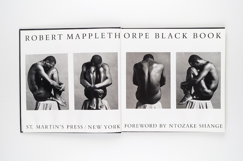 May include: An open book titled "ROBERT MAPPLETHORPE BLACK BOOK" with black and white photographs of a person in various poses. The book is open, displaying four images. The text "ST. MARTIN'S PRESS / NEW YORK FOREWORD BY NTOZAKE SHANGE" is also visible.