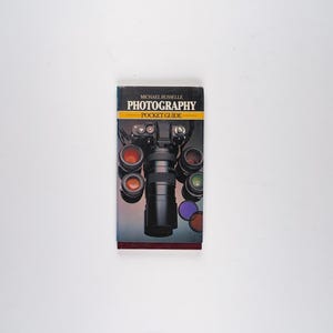 May include: A black and yellow pocket guide titled "Photography" by Michael Busselle. The cover features a camera lens and several other lenses.