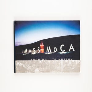 May include: A book cover with the text "MASS MoCA" in white letters, with a colorful image of a building and a blue sky. The text "FROM MILL TO MUSEUM" is below the main text. The bottom half of the cover has a faded image of people.