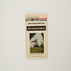 Könnte beinhalten: Ein Vintage-Reiseführer zum Fotografieren von Amsterdam mit einer Windmühle auf dem Cover. Der Reiseführer trägt den Titel "Amphoto Travel Guide photographing Amsterdam" und enthält den Text "A Guide for Photographers".