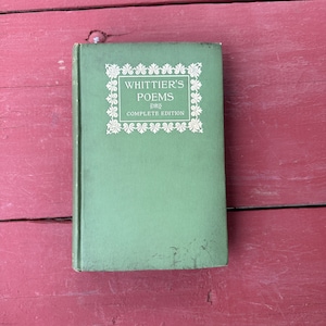 May include: A green hardcover book with the title "Whittier's Poems Complete Edition" in white lettering within a decorative white frame.