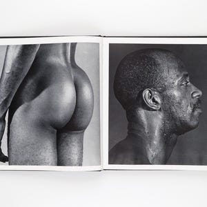 May include: A monochrome photograph of an open book. One page shows a person's rear, the other a profile of a person's face and neck. The images are in black and white.