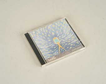 Può includere: Un'immagine di un CD con un'illustrazione stravagante. L'opera raffigura una figura gialla con le braccia tese su uno sfondo di motivi blu e gialli. La custodia del CD ha un dorso nero e il testo "Softla & Friends".