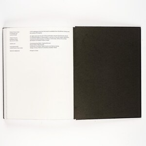 May include: An open book with a black cover and white pages. The left page has text, while the right page is solid black. The book is on a white surface.