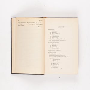 May include: An open book with a black cover, displaying the preface and table of contents. The pages are off-white with black text. The book is on a white surface.