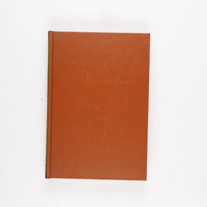 May include: A hardcover book with a solid, reddish-brown cover. The book is rectangular and appears to be closed, with the spine visible on the left side. The background is plain white.