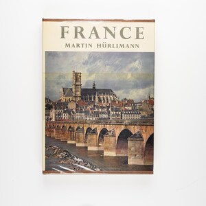 Pode incluir: Uma capa de livro vintage com o título "FRANCE" e o autor "MARTIN HÜRLIMANN". A capa apresenta uma pintura de uma ponte sobre um rio com uma cidade ao fundo.