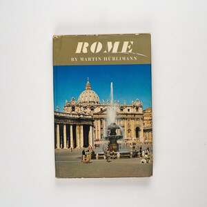 Pode incluir: Um livro vintage intitulado "ROMA" de Martin Hürlimann, com uma foto da Basílica de São Pedro e uma fonte em primeiro plano.