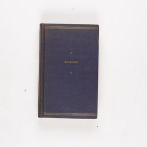 May include: A hardcover book with a dark blue cover and gold lettering. The title "Emerson" is printed in gold on the front. Gold lines border the top and bottom of the cover. The book is on a white background.