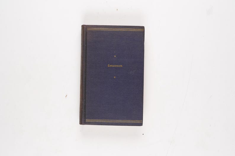 May include: A hardcover book with a dark blue cover and gold lettering. The title "Emerson" is printed in gold on the front. Gold lines border the top and bottom of the cover. The book is on a white background.