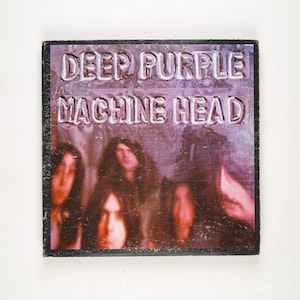 May include: Album cover for Deep Purple's Machine Head. The album art features the band's name and album title in embossed white lettering. The background is a blurry image of the band members in shades of purple and red.