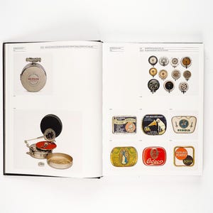 May include: A book spread featuring vintage audio equipment. The left page displays a silver-toned, circular music player and a phonograph. The right page showcases various speaker components and colorful, rectangular labels with illustrations.