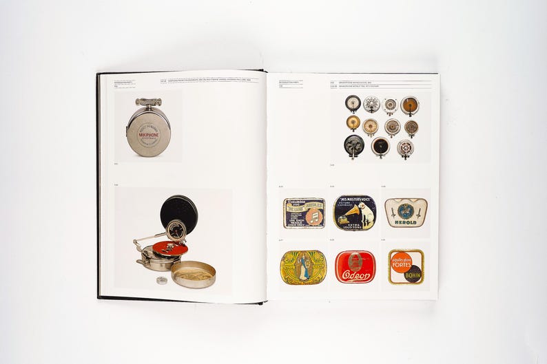 May include: A book spread featuring vintage audio equipment. The left page displays a silver-toned, circular music player and a phonograph. The right page showcases various speaker components and colorful, rectangular labels with illustrations.
