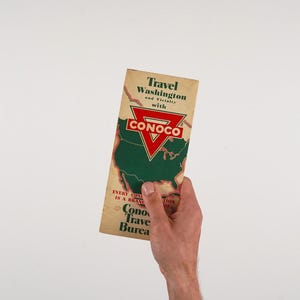 May include: A vintage travel brochure for Washington state, featuring a green map of the U.S. and the Conoco logo. The brochure's text includes "Travel Washington" and "Conoco Travel Bureau."