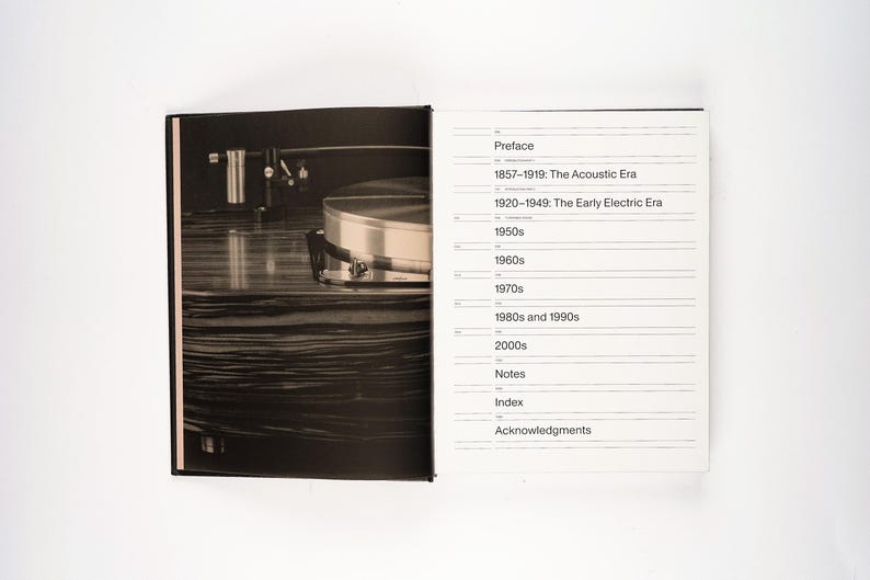 May include: A black and white photograph of an open book. The left page features a close-up of a record player. The right page displays a table of contents with the headings: Preface, 1857-1919: The Acoustic Era, and other decades.