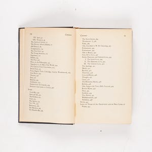 May include: An open book with a black cover, displaying two cream-colored pages filled with text. The left page lists chapter titles, while the right page shows a table of contents. The book is set against a white background.
