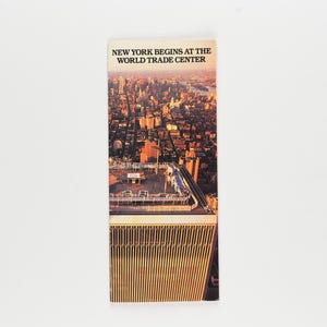 May include: A rectangular brochure featuring a high-angle aerial photograph of the New York City skyline at sunset. The text at the top reads, NEW YORK BEGINS AT THE WORLD TRADE CENTER, positioned above the building's roof and city grid.