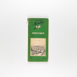 May include: A vintage green Michelin travel guide for Provence, France. The cover features the Michelin logo, the word "PROVENCE," and a black and white illustration of an aqueduct. The guide is slightly worn, with a visible crease.
